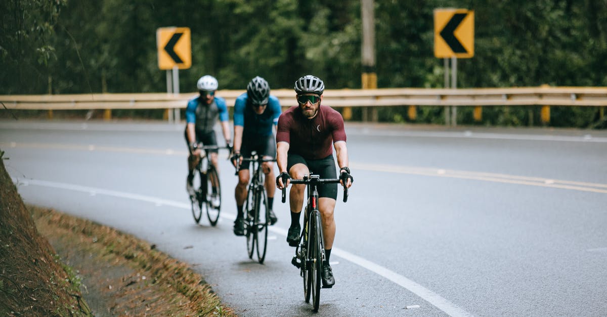 Need cycling route options from Bangkok to Siem Reap (via Poi Pet) [closed] - Anonymous male cyclists in sportswear and helmets riding bicycles on fenced asphalt roadway in summer