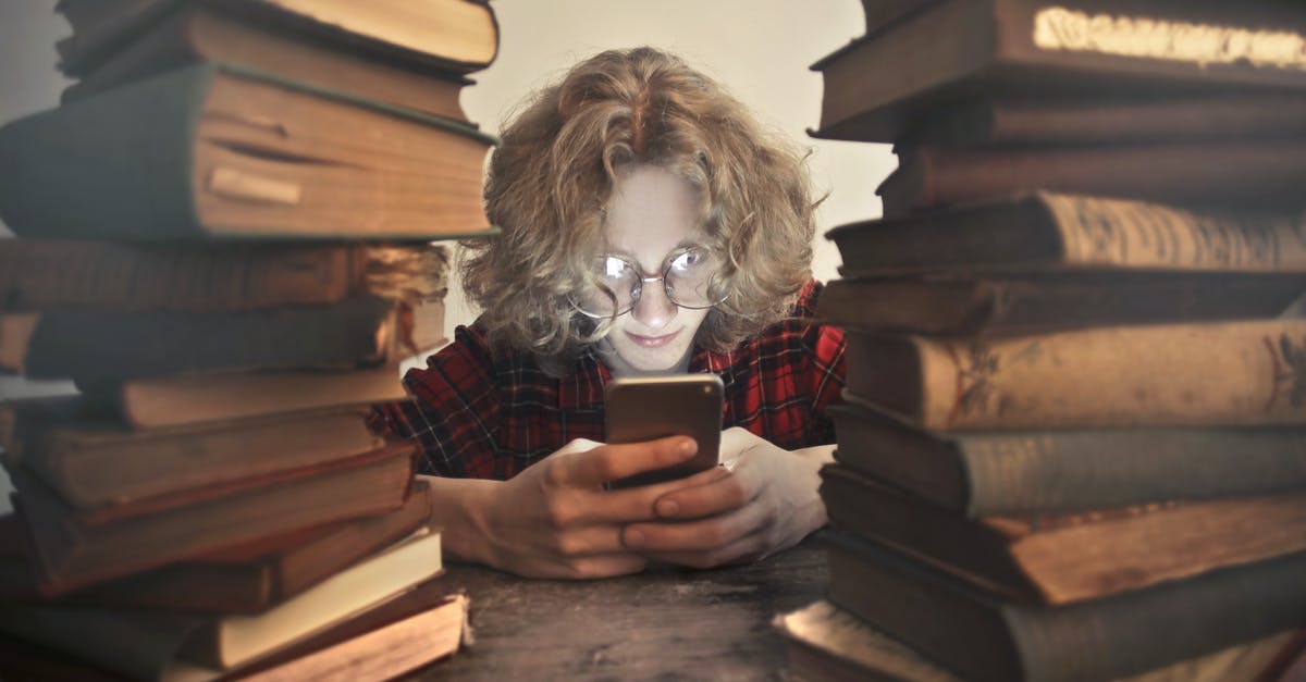Nigerian citizen (university student) was refused a UK visit visa due to lack of funds and connection to school - how to resolve? - Focused male student in casual wear and glasses browsing smartphone while sitting at wooden table with stacked old books