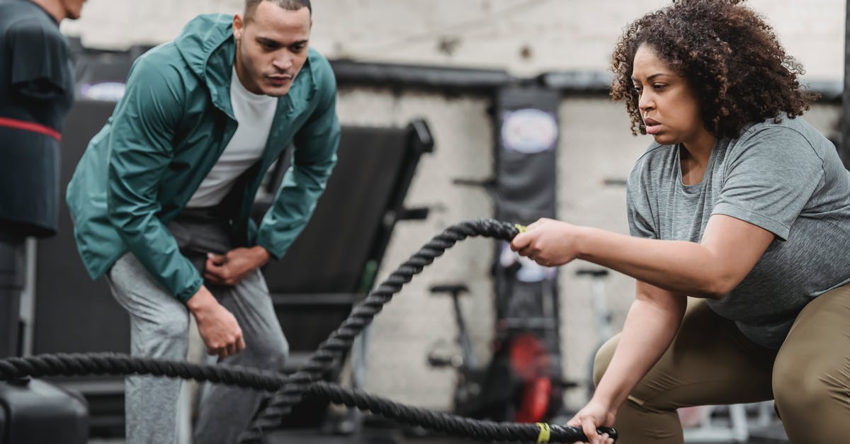 No coach offered to Colorado Springs on American Airlines? - Plus sized African American female in sportswear exercising with battle ropes near serious male instructor during intense workout in modern fitness center