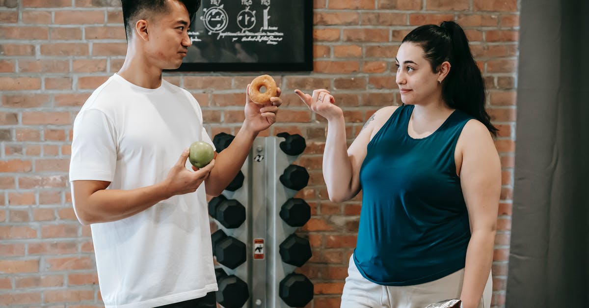 No coach offered to Colorado Springs on American Airlines? - Side view of Asian personal instructor with apple and doughnut offering healthy food to plus size woman while standing in gym