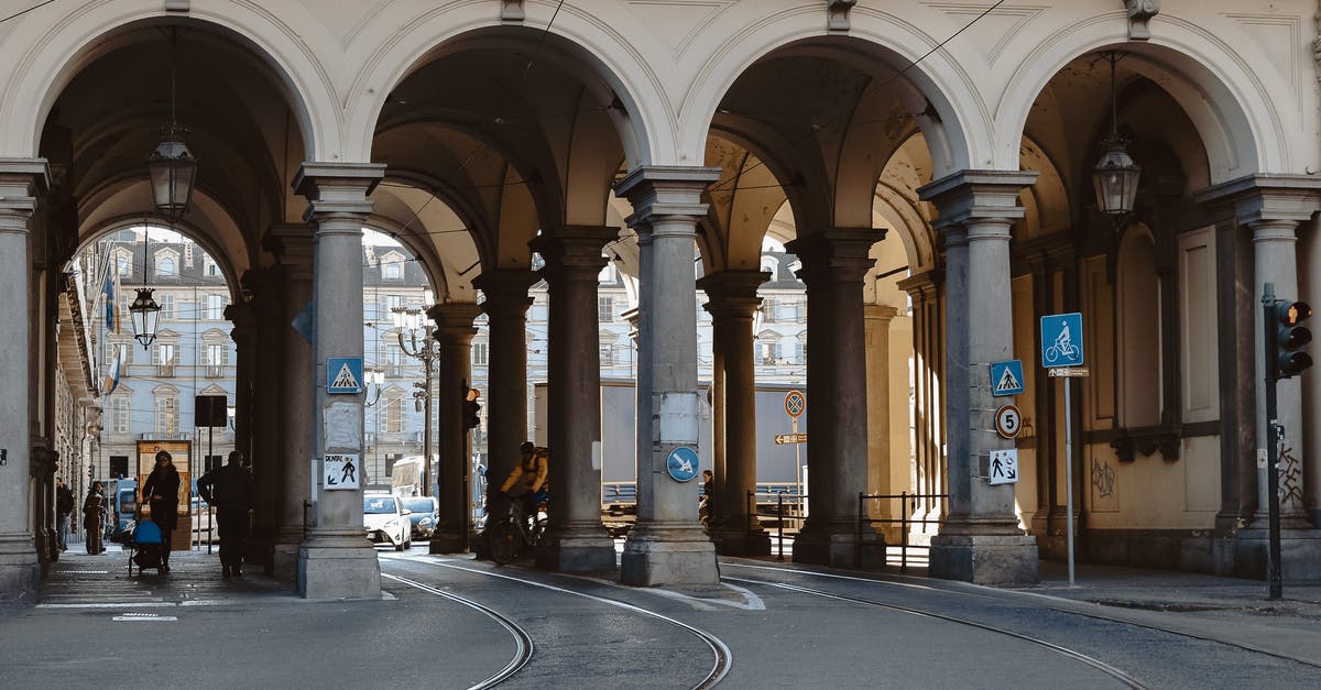 Non-EU citizen in Europe - Unrecognizable citizens on asphalt roadway with tram rails under aged masonry construction with arches and colonnade in city Non-EU citizen in Europe - Unrecognizable citizens on asphalt roadway with tram rails under aged masonry construction with arches and colonnade in city