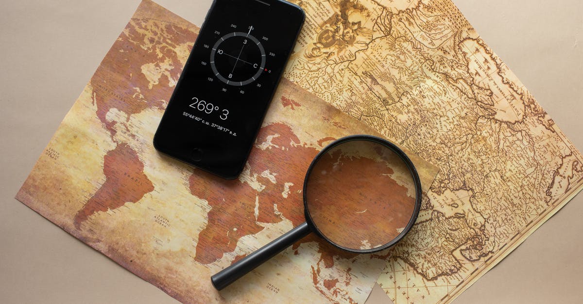 obtain UK visa from Egypt and travel from another country - Top view of magnifying glass and cellphone with compass with coordinates placed on paper maps on beige background in light room