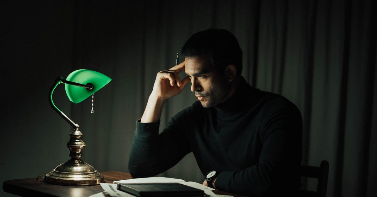 Occupancy rate and late reservations - Side view of pensive male with pen doing paperwork while sitting at wooden desktop with vintage table lamp during work in obscure room Occupancy rate and late reservations - Side view of pensive male with pen doing paperwork while sitting at wooden desktop with vintage table lamp during work in obscure room