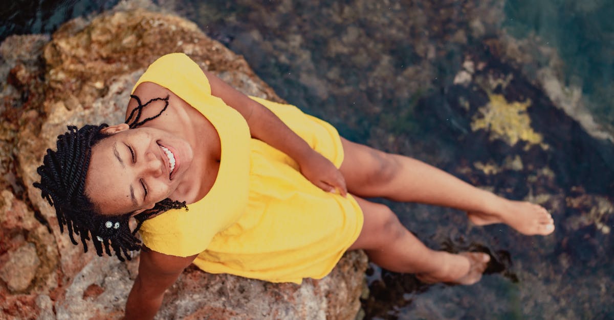 On budget travel from Orlando Florida to Lake Charles LA [closed] - From above of young content barefoot ethnic female tourist with closed eyes in trendy wear sitting on cliff near pond