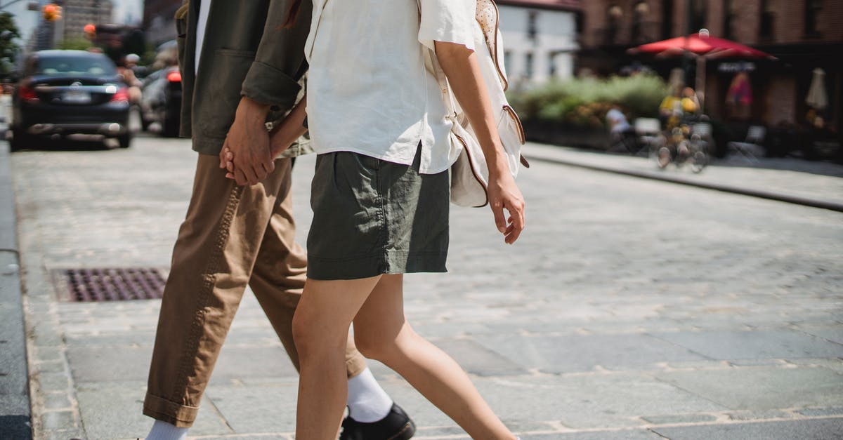 One Way Car Rental in Italy - Romantic idea or completely mad? - Side view of unrecognizable couple holding hands and crossing road on sunny street in city with blurred cars and buildings One Way Car Rental in Italy - Romantic idea or completely mad? - Side view of unrecognizable couple holding hands and crossing road on sunny street in city with blurred cars and buildings