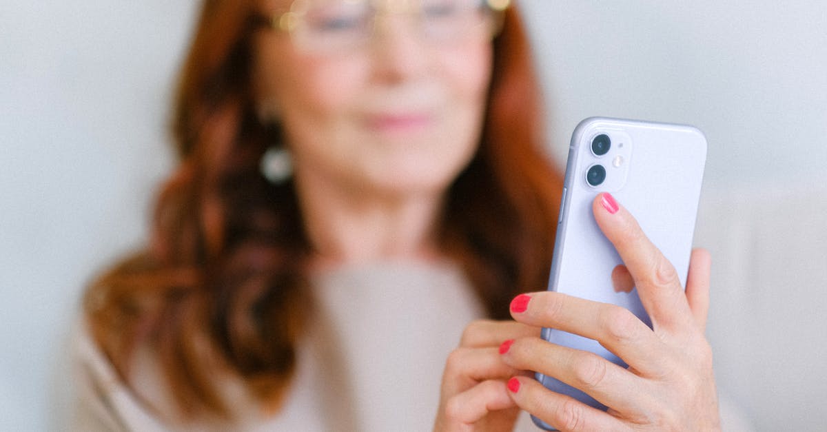 Online check-in not permitted due to my nationality? - Crop aged redhead female in eyeglasses using contemporary mobile phone while surfing internet in soft focus