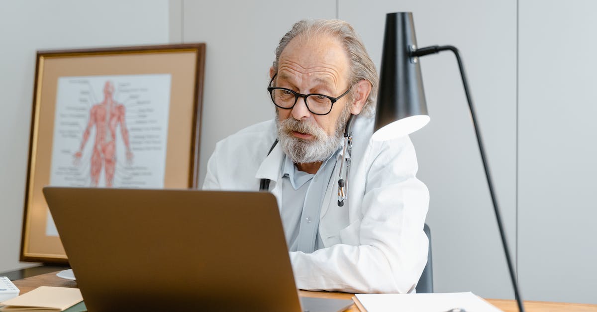 Online medical insurance for short visa in Romania - An Elderly Man in White Lab Coat Talking while Facing the Laptop Online medical insurance for short visa in Romania - An Elderly Man in White Lab Coat Talking while Facing the Laptop