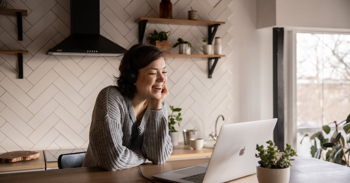 Online resource for duty-free - Young cheerful female smiling and talking via laptop while sitting at wooden table in cozy kitchen Online resource for duty-free - Young cheerful female smiling and talking via laptop while sitting at wooden table in cozy kitchen
