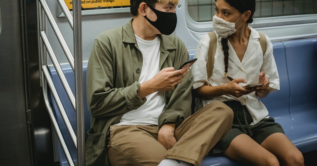 Online resource for reconnecting with other travelers? - Unrecognizable young Asian man and ethnic woman in face masks and casual clothes using mobile phones and chatting while riding train Online resource for reconnecting with other travelers? - Unrecognizable young Asian man and ethnic woman in face masks and casual clothes using mobile phones and chatting while riding train