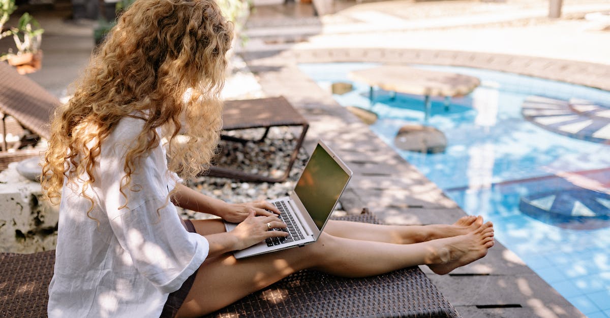 Online resource for reconnecting with other travelers? - From above side view of unrecognizable barefoot female traveler with curly hair typing on netbook while resting on sunbed near swimming pool on sunny day Online resource for reconnecting with other travelers? - From above side view of unrecognizable barefoot female traveler with curly hair typing on netbook while resting on sunbed near swimming pool on sunny day