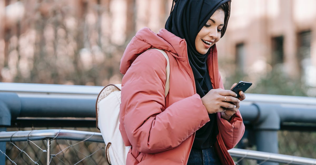 Online ticketing of National Express buses in UK - Muslim ethnic female in hijab texting message on mobile phone near iron construction on blurred background of building Online ticketing of National Express buses in UK - Muslim ethnic female in hijab texting message on mobile phone near iron construction on blurred background of building