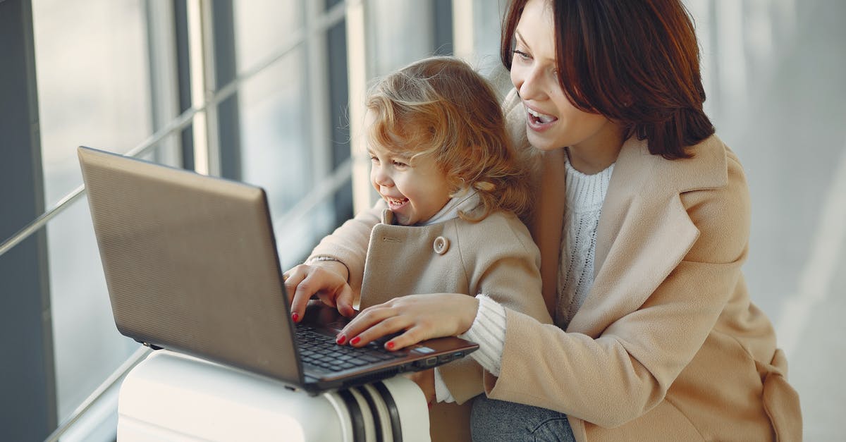 Only allowed to travel to connecting airport - Cheerful stylish woman with suitcase hugging adorable laughing daughter and browsing laptop together while waiting for flight in airport hallway Only allowed to travel to connecting airport - Cheerful stylish woman with suitcase hugging adorable laughing daughter and browsing laptop together while waiting for flight in airport hallway