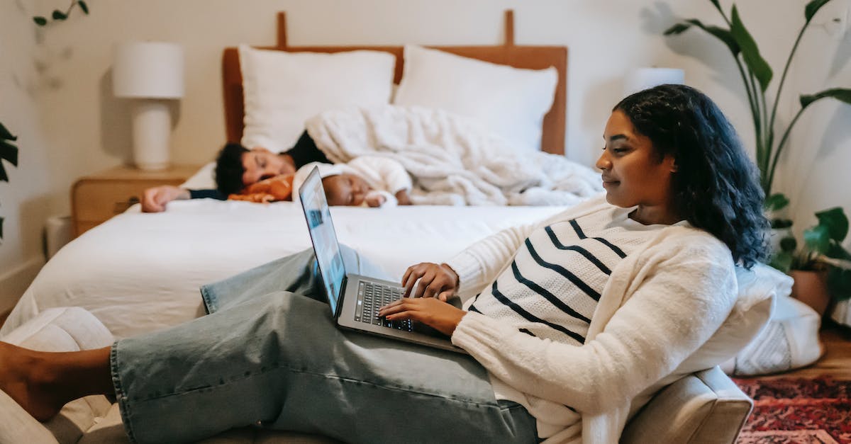 Overnight connection in Guangzhou - where do I sleep? - Side view of pensive ethnic woman freelancer sitting on couch and browsing netbook while man and little baby sleeping on bed in cozy bedroom Overnight connection in Guangzhou - where do I sleep? - Side view of pensive ethnic woman freelancer sitting on couch and browsing netbook while man and little baby sleeping on bed in cozy bedroom