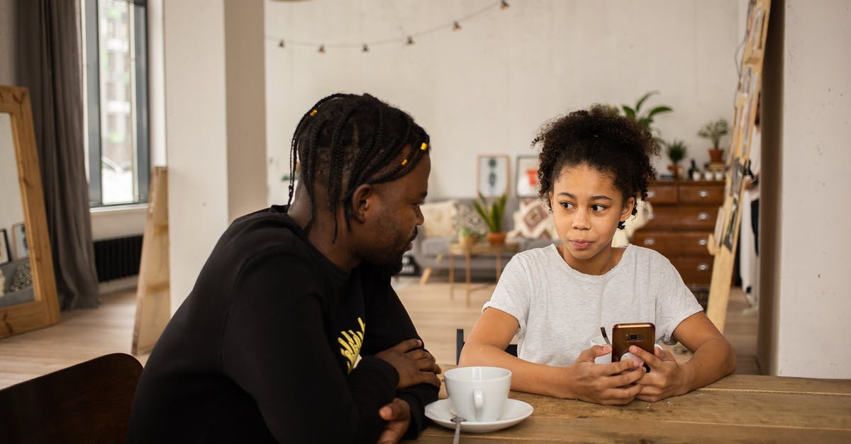 Parent-child; sit next to each other on an all-inclusive flight? - African American man sitting at table with cup of coffee and talking to daughter browsing cellphone Parent-child; sit next to each other on an all-inclusive flight? - African American man sitting at table with cup of coffee and talking to daughter browsing cellphone