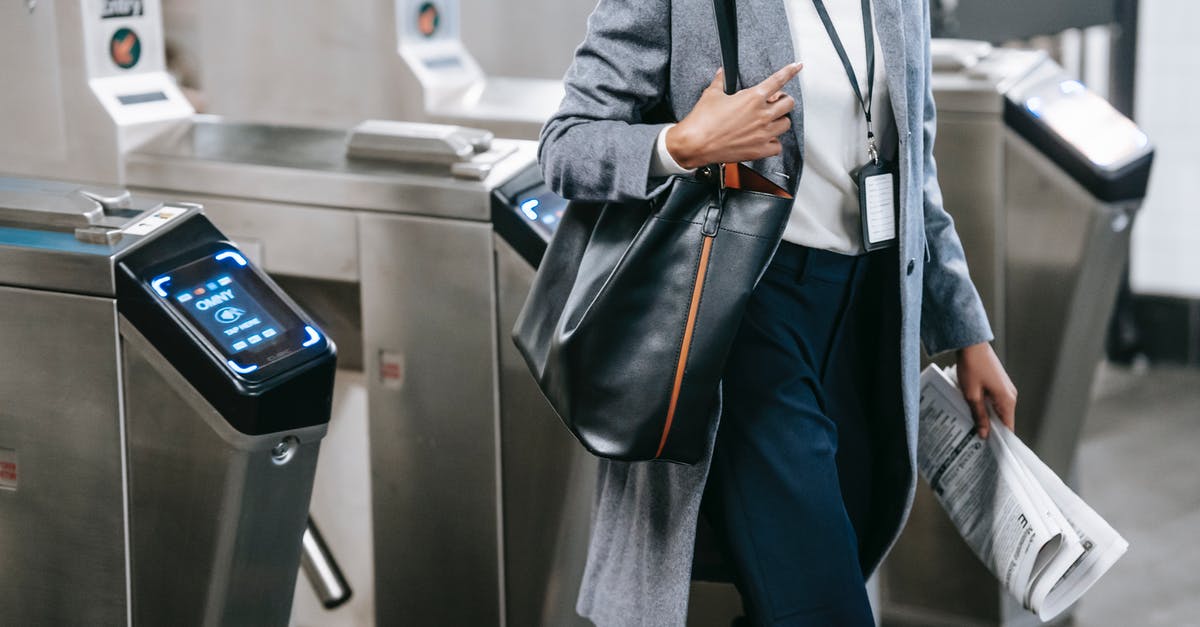 Pass for public transport in San Francisco - Crop anonymous African American female in formal clothes with newspaper passing through turnstile gates in modern underground station Pass for public transport in San Francisco - Crop anonymous African American female in formal clothes with newspaper passing through turnstile gates in modern underground station