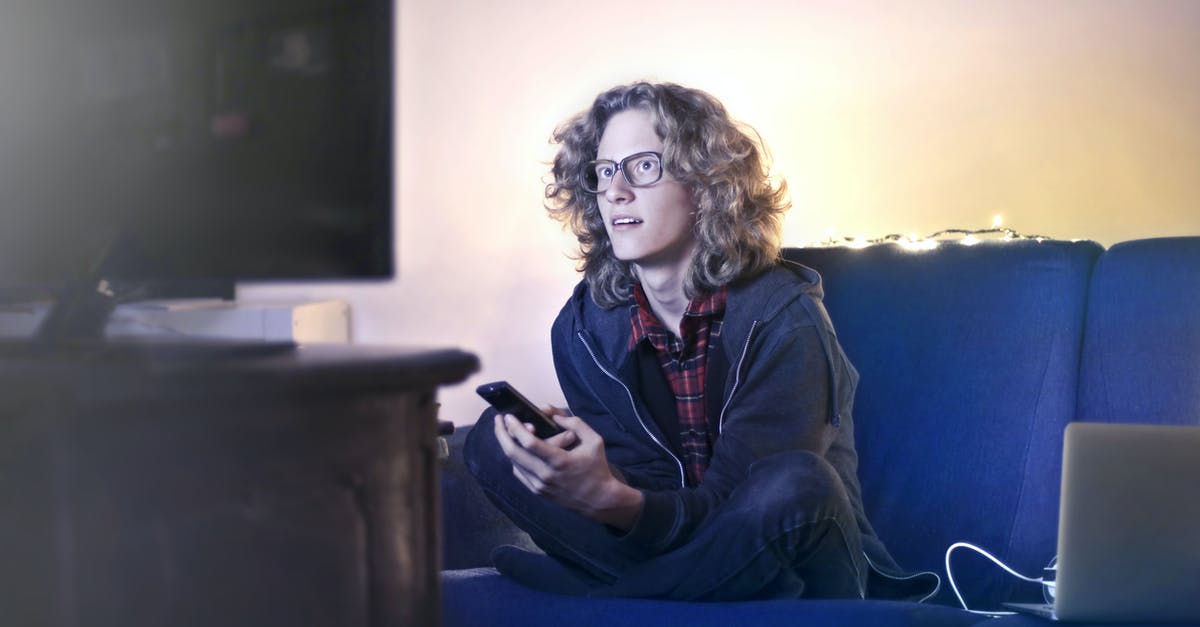 Photographable location from "Gangnam Style" music video - Concentrated male with long hair sitting on comfortable sofa at home and messaging on social media via cellphone while watching movie on TV with opened mouth Photographable location from "Gangnam Style" music video - Concentrated male with long hair sitting on comfortable sofa at home and messaging on social media via cellphone while watching movie on TV with opened mouth