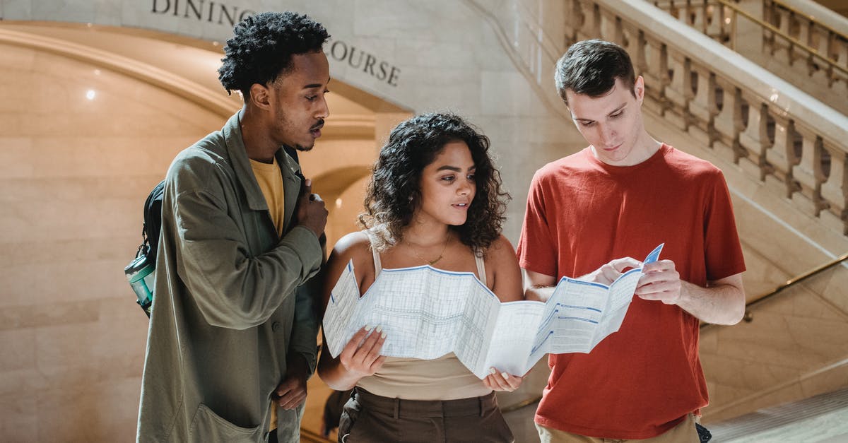 Pick up point for Shuttle from Terminal 8 JFK - Focused young man pointing at map while searching for route with multiracial friends in Grand Central Terminal during trip in New York