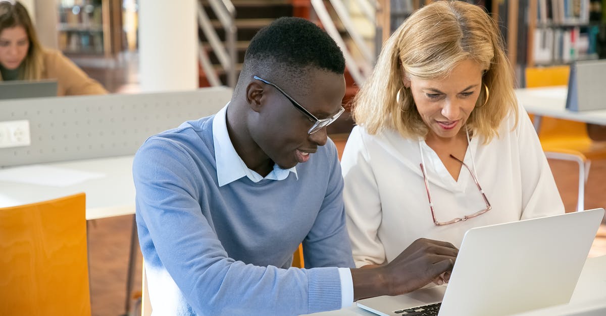 Please explain the local library system in London, England - Female teacher helping ethnic male student working on laptop in library Please explain the local library system in London, England - Female teacher helping ethnic male student working on laptop in library