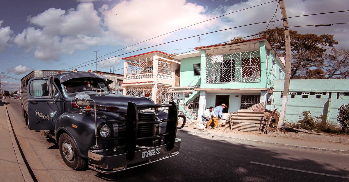 Post forwarding in the UK - Aged pickup vehicle on rough roadway against building facade and unrecognizable ethnic partners under blue cloudy sky in town Post forwarding in the UK - Aged pickup vehicle on rough roadway against building facade and unrecognizable ethnic partners under blue cloudy sky in town