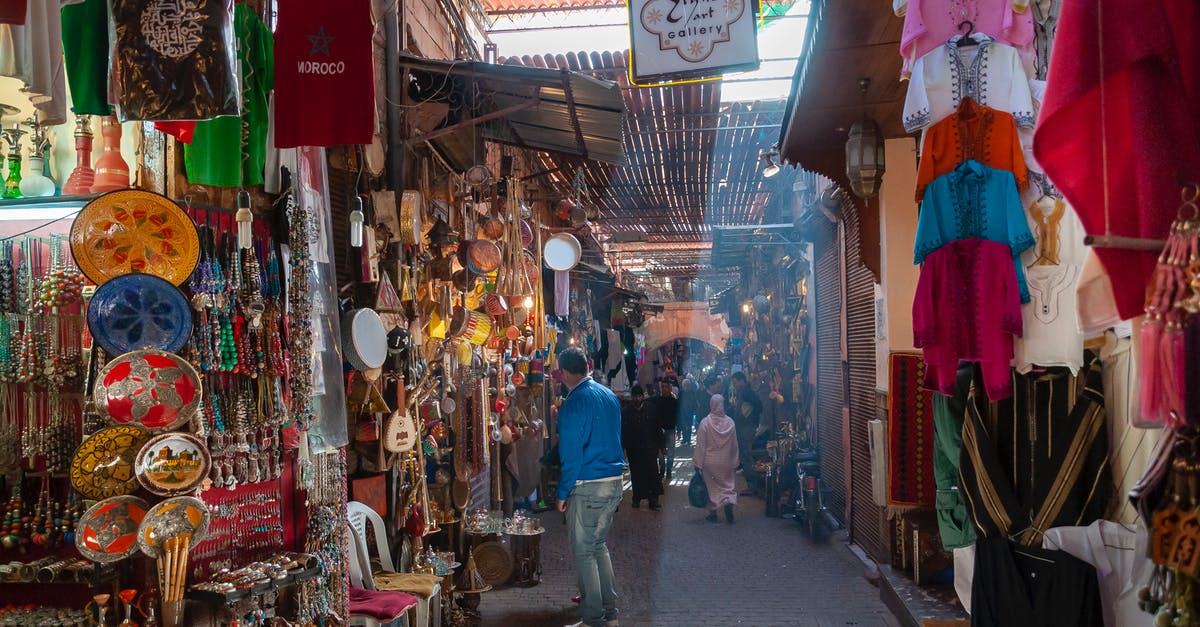 Precautions and Customs to observe when traveling in Morocco - Unrecognizable people walking in local bazaar near stalls with various goods and souvenirs and traditional clothes on sunny day in Marrakesh Precautions and Customs to observe when traveling in Morocco - Unrecognizable people walking in local bazaar near stalls with various goods and souvenirs and traditional clothes on sunny day in Marrakesh
