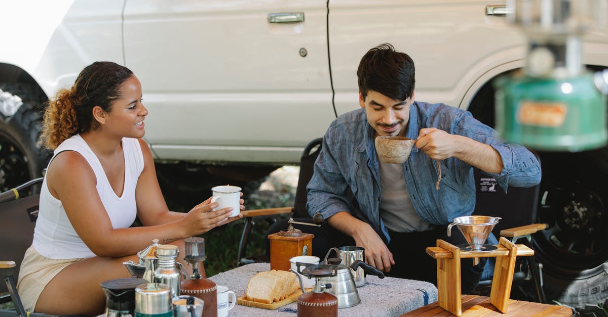 Processing a visa application with a past expected travel date - Positive diverse couple drinking delicious pour over coffee in campsite Processing a visa application with a past expected travel date - Positive diverse couple drinking delicious pour over coffee in campsite