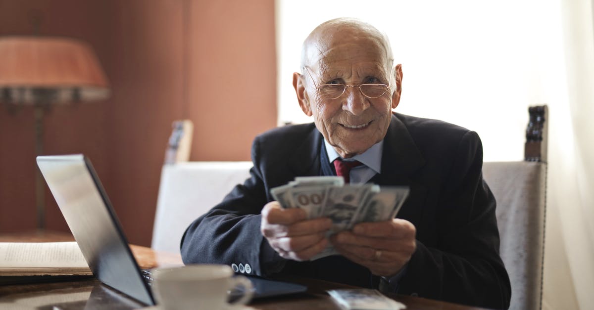 Proof of income for UK visitor visa - Confident senior businessman holding money in hands while sitting at table near laptop Proof of income for UK visitor visa - Confident senior businessman holding money in hands while sitting at table near laptop