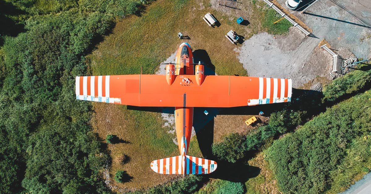 Proof of onward travel by flight from another country - Aerial view of colorful orange airplane on green meadow in countryside in sunlight Proof of onward travel by flight from another country - Aerial view of colorful orange airplane on green meadow in countryside in sunlight