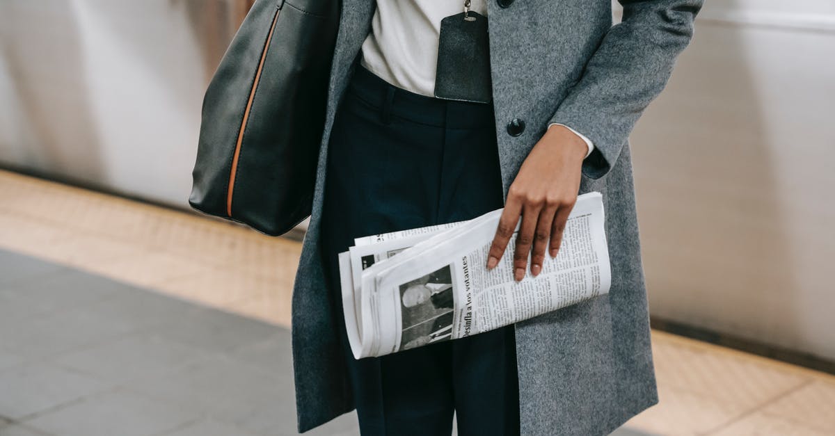 Public transports from Prague to Wroclaw - From above of crop anonymous female employee in elegant outfit and name tag standing on platform of metro station with newspaper in hand