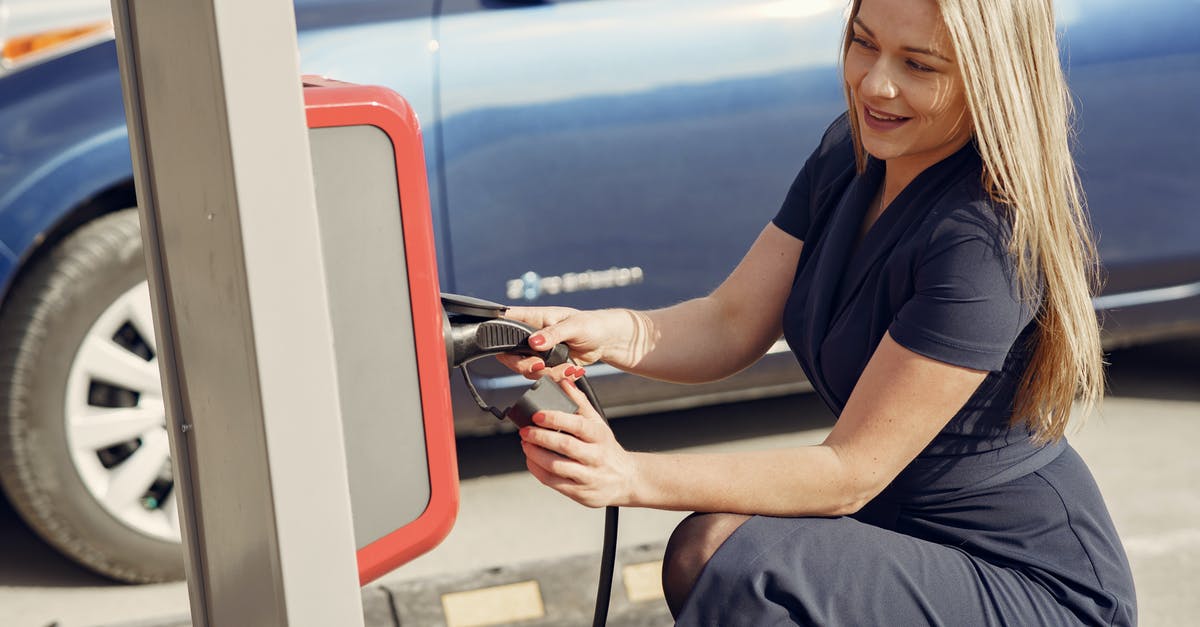 Publicly-accessible electric sockets in Munich to charge dead devices? - Side view of positive female in casual dress sitting near station on street charging electric vehicle for continuation trip Publicly-accessible electric sockets in Munich to charge dead devices? - Side view of positive female in casual dress sitting near station on street charging electric vehicle for continuation trip