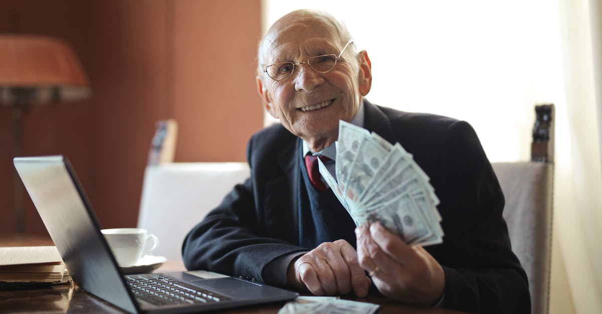 Putting a hold on an airline seat - Happy senior businessman holding money in hand while working on laptop at table Putting a hold on an airline seat - Happy senior businessman holding money in hand while working on laptop at table
