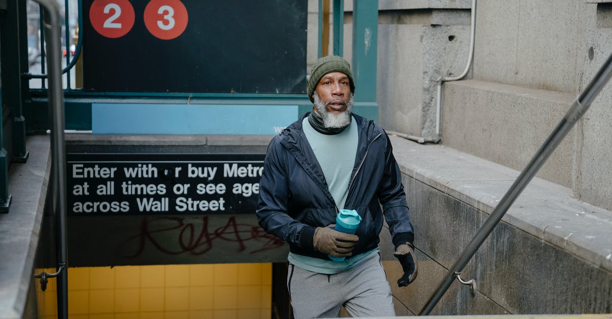 Quick way to exit King's Cross tube station? - Thoughtful senior African American male in warm jacket and knitted hat and gloves and fitness bottle in hand going upstairs from underground passage of subway station Quick way to exit King's Cross tube station? - Thoughtful senior African American male in warm jacket and knitted hat and gloves and fitness bottle in hand going upstairs from underground passage of subway station