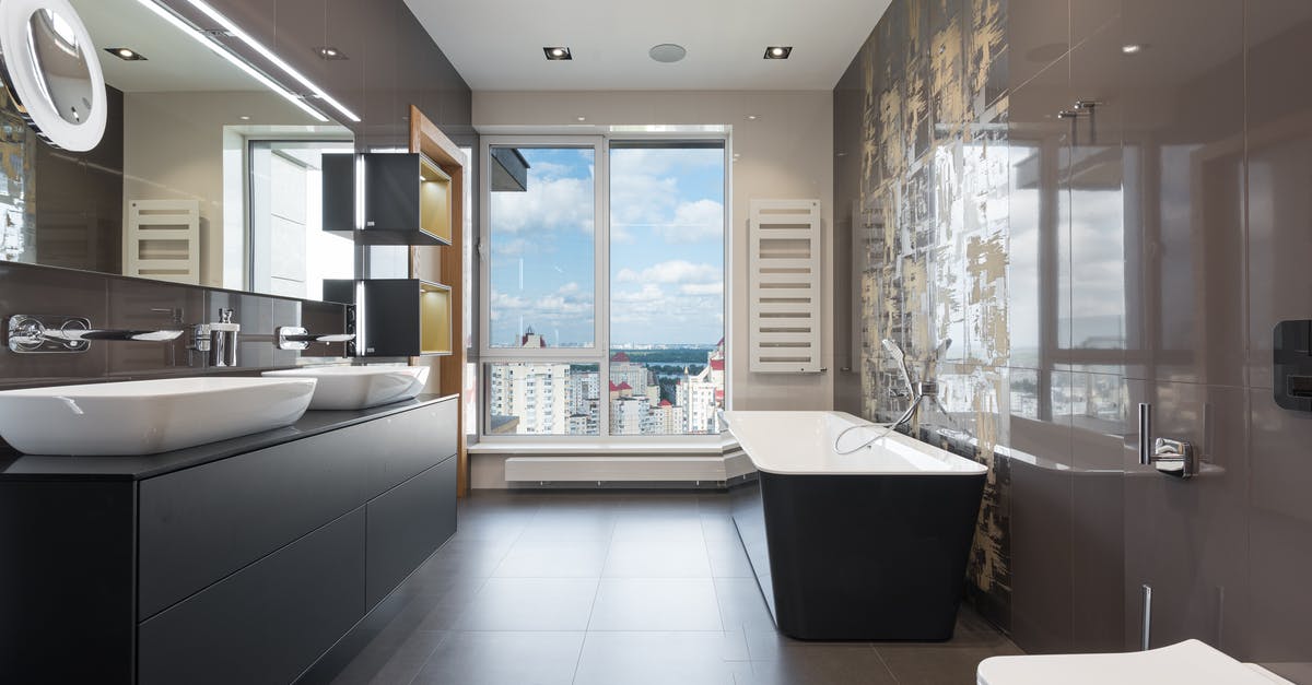Quietest bath & times in budapest - Wooden furniture with bathtub and ceramic sinks and toilet bowl in contemporary master bathroom with big windows in daylight Quietest bath & times in budapest - Wooden furniture with bathtub and ceramic sinks and toilet bowl in contemporary master bathroom with big windows in daylight
