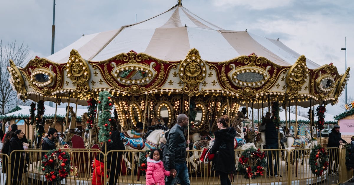 "Park and Ride" options to visit London? - Side view of black father with girl passing by glowing carousel in city fairground on gloomy day "Park and Ride" options to visit London? - Side view of black father with girl passing by glowing carousel in city fairground on gloomy day