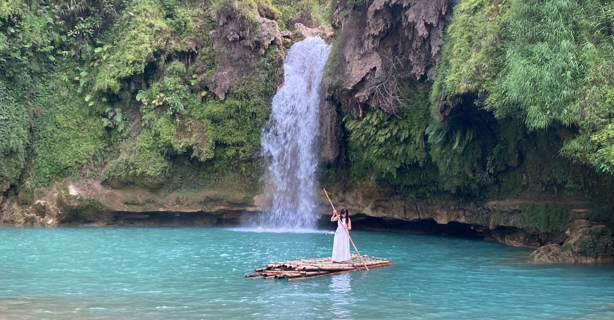 Raft trip down a river - Woman floating on raft with oar against waterfall Raft trip down a river - Woman floating on raft with oar against waterfall
