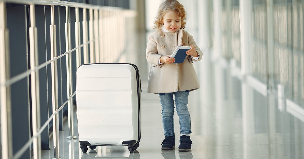 Re-checking luggage at connecting airports - Full body of smiling cute little girl in jeans and beige coat standing near suitcase and checking information in documents Re-checking luggage at connecting airports - Full body of smiling cute little girl in jeans and beige coat standing near suitcase and checking information in documents