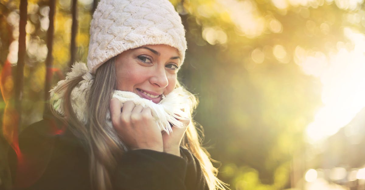Rent clothing in Frankfurt / Being warm without cold weather clothing - Young content female wearing warm hat and scarf standing in city garden and enjoying weekend while smiling and looking at camera Rent clothing in Frankfurt / Being warm without cold weather clothing - Young content female wearing warm hat and scarf standing in city garden and enjoying weekend while smiling and looking at camera