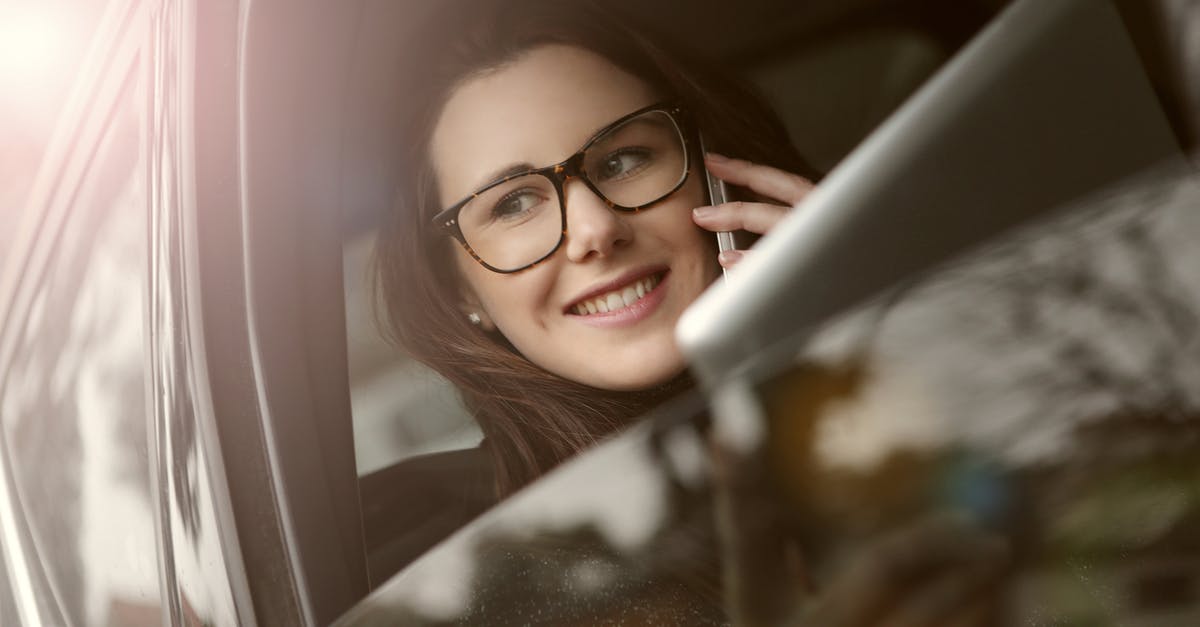Renting a car from private persons in California - Female in glasses with tablet talking on smartphone while sitting in car with opened window Renting a car from private persons in California - Female in glasses with tablet talking on smartphone while sitting in car with opened window