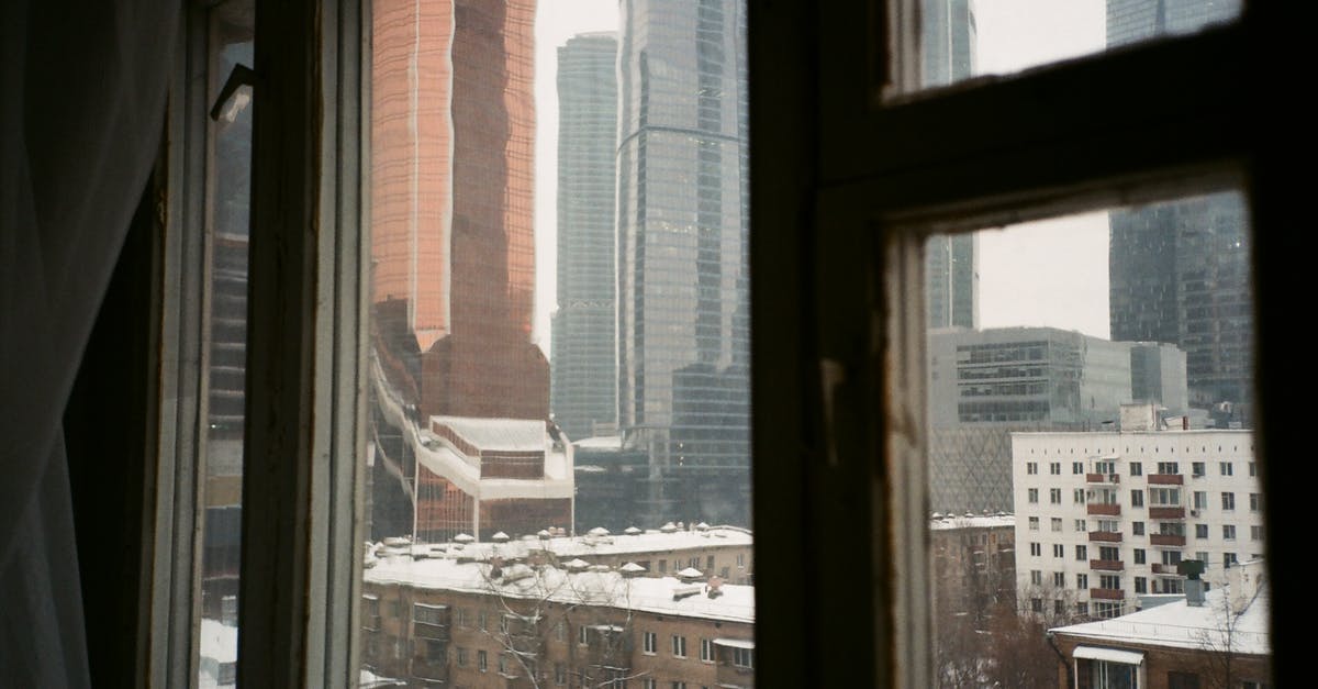 Renting a flat or rooms in the Alps area for winter season [closed] - Through apartment window view of modern urban city architecture with snowy residential buildings and skyscrapers on overcast winter day