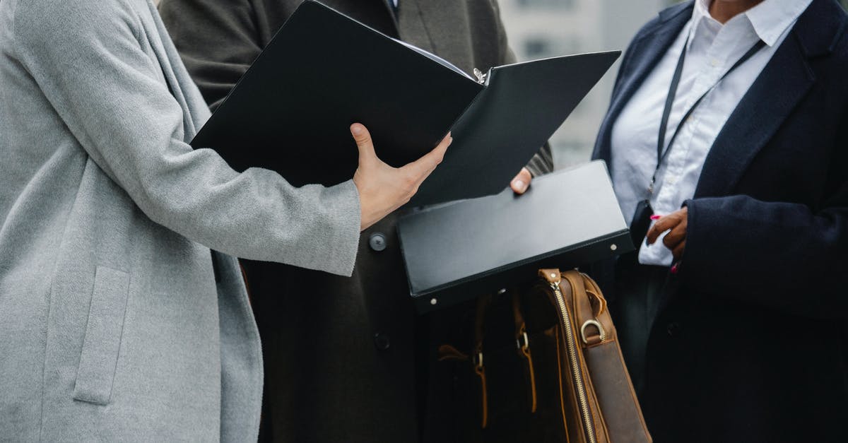 Required visa for work-at-home (abroad) person visiting his/her employer in US - Crop diverse coworkers wearing formal outfits reading documents together and discussing project on street Required visa for work-at-home (abroad) person visiting his/her employer in US - Crop diverse coworkers wearing formal outfits reading documents together and discussing project on street