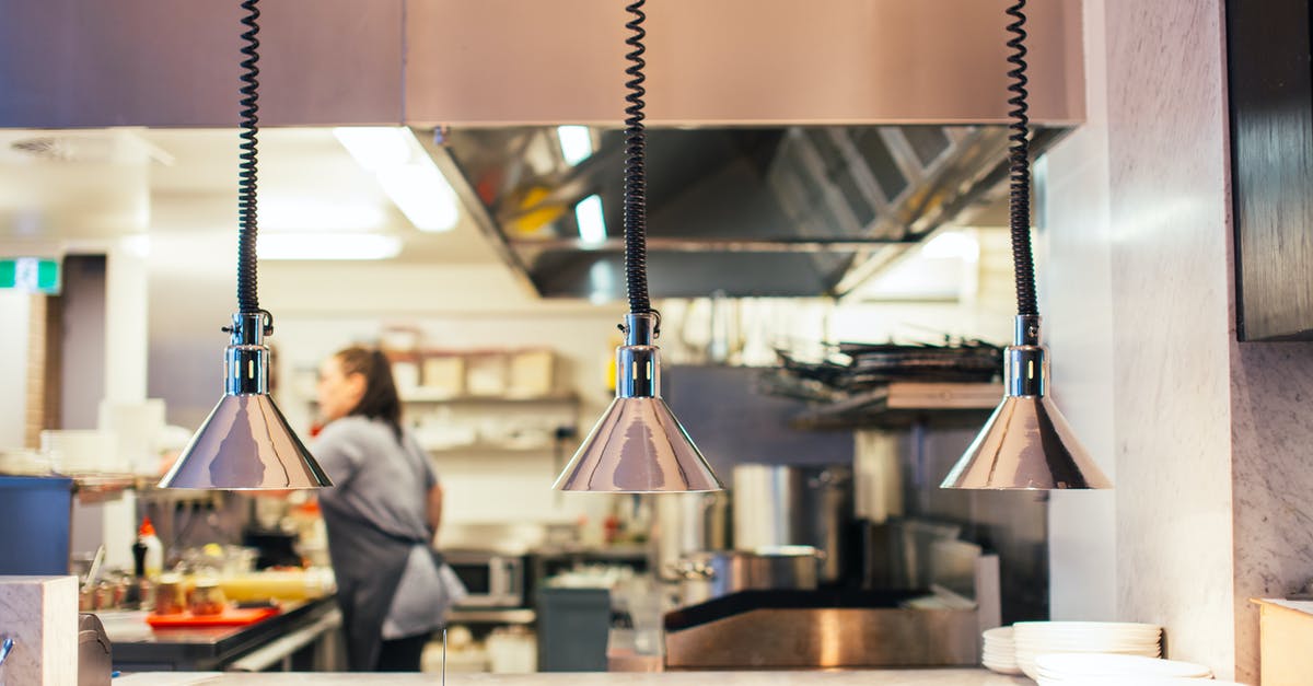 Restaurant in Paris decorated in kitchen utensils - Side view of unrecognizable female chef in restaurant kitchen working behind counter with infrared lamps and serving kitchenware Restaurant in Paris decorated in kitchen utensils - Side view of unrecognizable female chef in restaurant kitchen working behind counter with infrared lamps and serving kitchenware