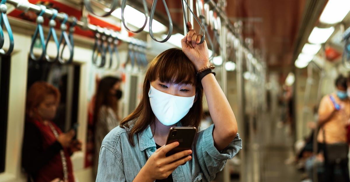 Retaining access to email when traveling - Woman Wearing a Face Mask on the Subway and Using her Smartphone Retaining access to email when traveling - Woman Wearing a Face Mask on the Subway and Using her Smartphone