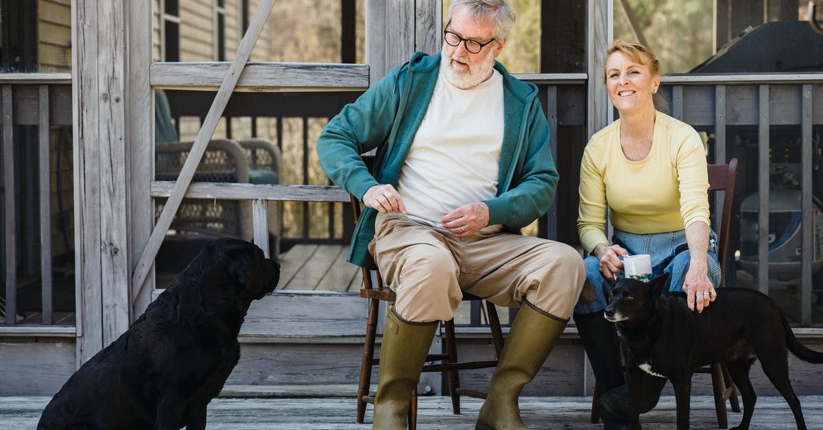 Retired couple wishing to spend more time in owned USA property [closed] - Delightful senior couple in rain boots sitting on chairs with black dogs while spending time together on terrace