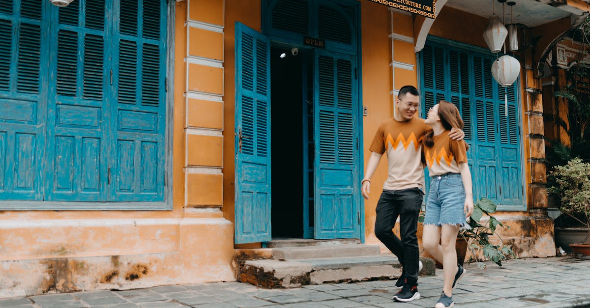 Return date earlier than Departure date on the same flight booking - Full length of happy Asian couple in same t shirts hugging and looking at each other while walking on street near entrance of colorful building