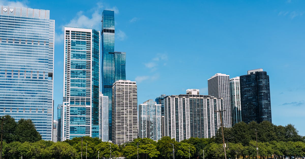 Returning to US after illegally working in the Schengen area - Exterior of modern glass skyscrapers built near lush city park under cloudless blue sky