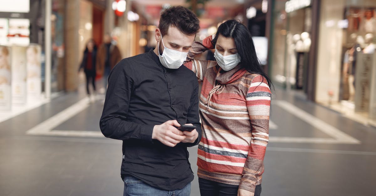 Risk of not turning Airplane Mode on, on a mobile device while in the air? - Focused young couple wearing medical masks with smartphone in shopping center Risk of not turning Airplane Mode on, on a mobile device while in the air? - Focused young couple wearing medical masks with smartphone in shopping center