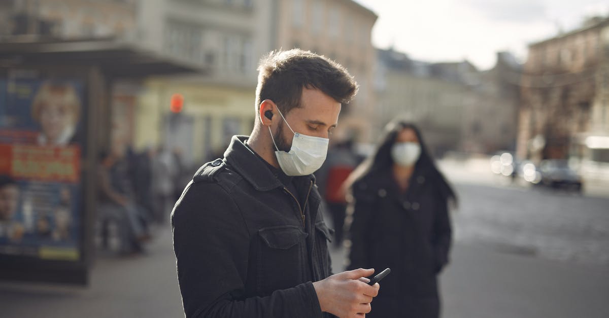 Risk of not turning Airplane Mode on, on a mobile device while in the air? - Focused man in medical mask using smartphone on urban street in cold season Risk of not turning Airplane Mode on, on a mobile device while in the air? - Focused man in medical mask using smartphone on urban street in cold season
