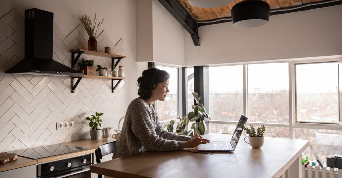 Risky Connection message - Side view of young female in casual clothes typing message on laptop while sitting at wooden table in kitchen Risky Connection message - Side view of young female in casual clothes typing message on laptop while sitting at wooden table in kitchen