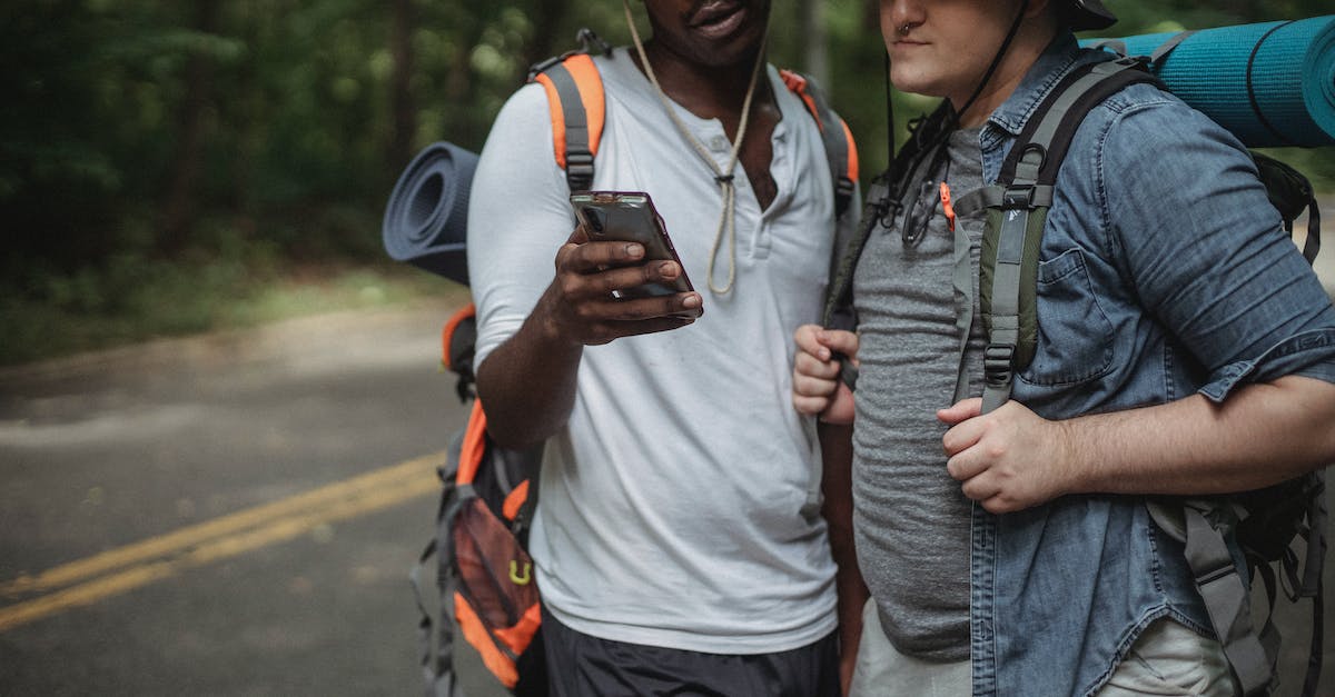 Road trip planner online - Crop diverse tourists with rucksacks watching smartphone on road Road trip planner online - Crop diverse tourists with rucksacks watching smartphone on road