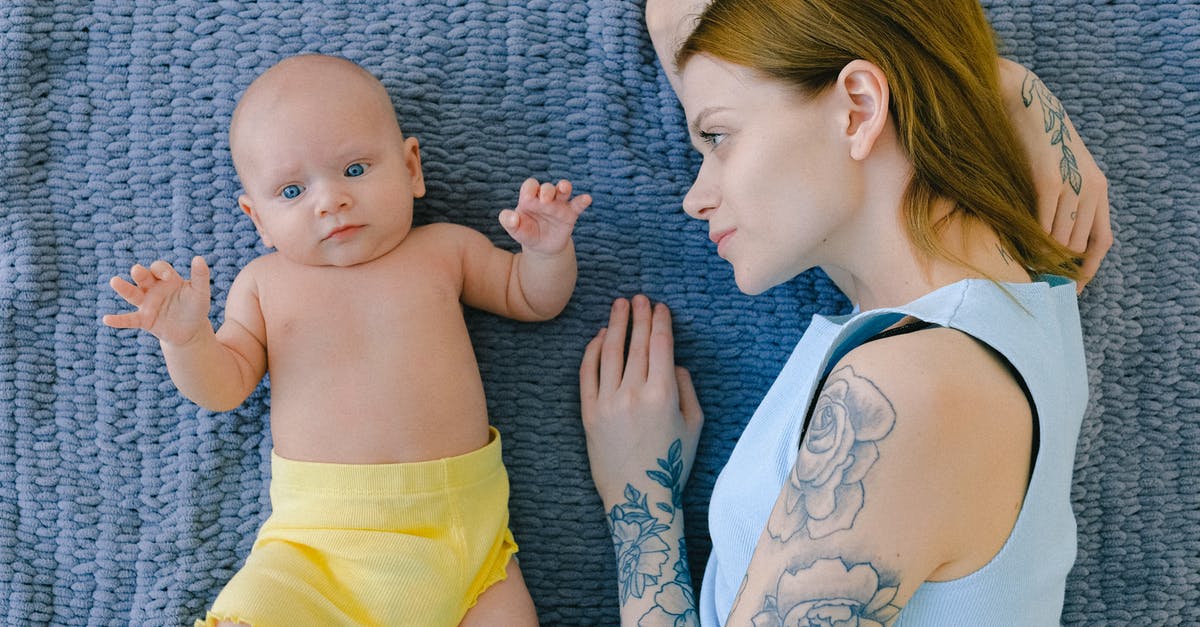 Russian mom traveling from US to Russian Federation with little kid [closed] - Top view of tattooed female in casual clothes looking at cute infant while resting together on soft blanket in room