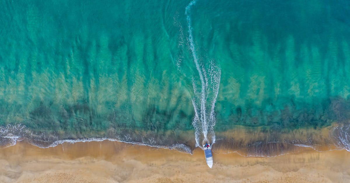 Sail boat from Santiago Chile to Tahiti - Drone view of calm sea water running on sandy remote sand with motorboat leaving trail while mooring Sail boat from Santiago Chile to Tahiti - Drone view of calm sea water running on sandy remote sand with motorboat leaving trail while mooring